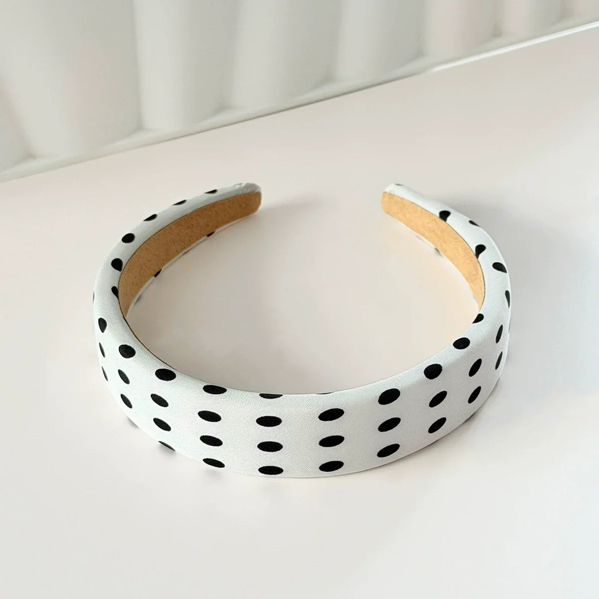 A white stretch hairband with black polka dots and a natural fiber band is shown on a white surface.