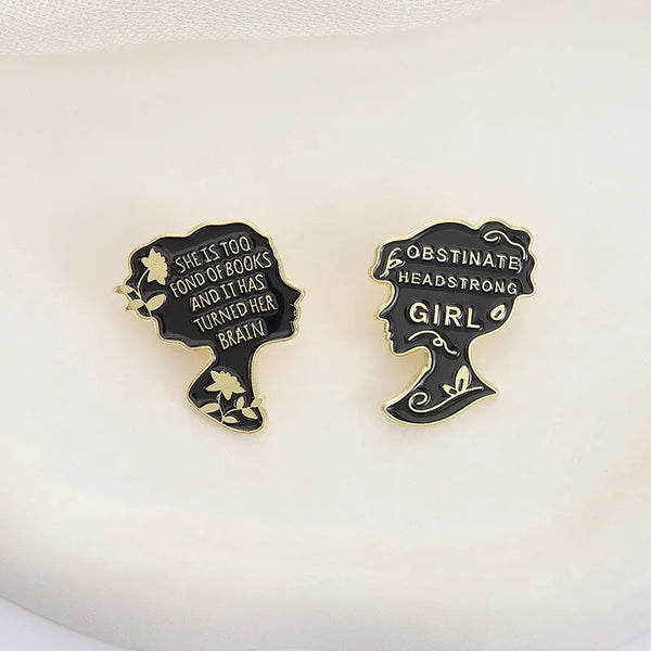 Two black enamel lapel pins shaped like female profiles with inspirational text