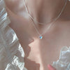 A delicate silver heart pendant necklace is worn against a sheer white blouse.