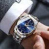 A close-up of a men's stainless steel quartz watch with a blue dial and gold accents worn on a wrist next to a suit cuff.
