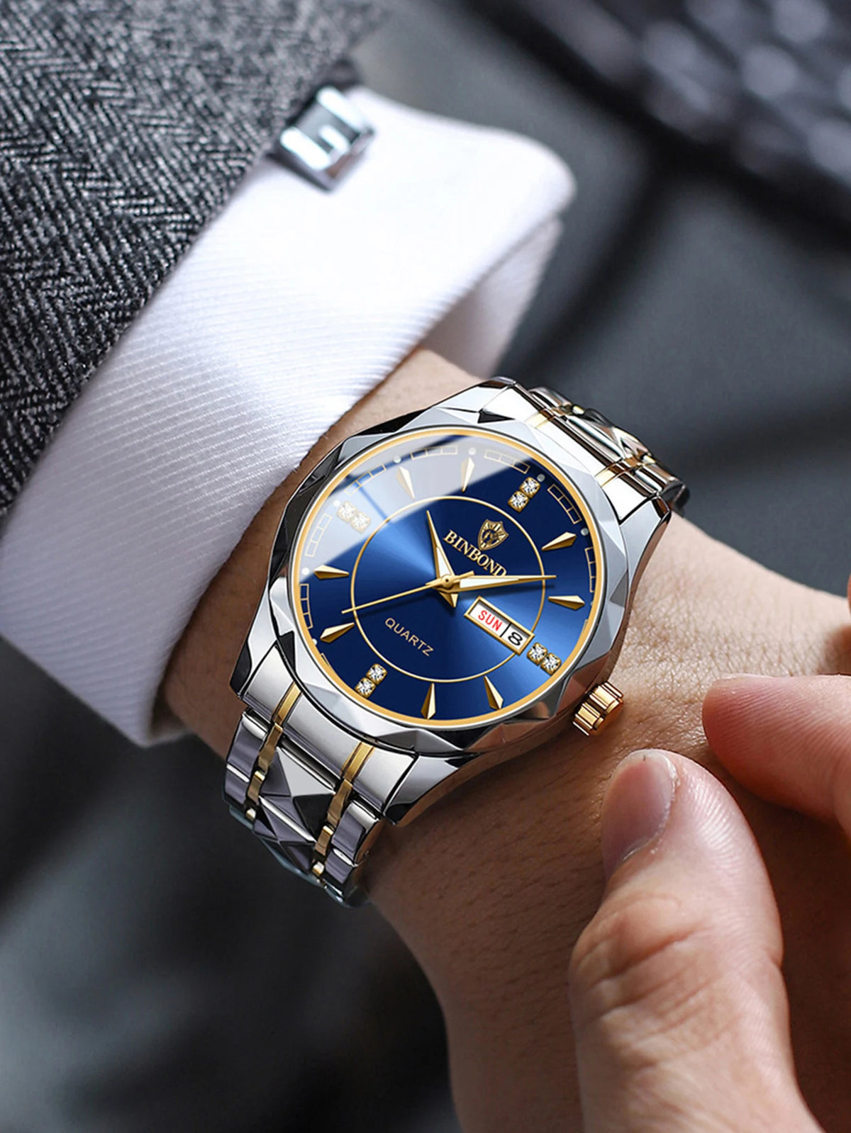 A close-up of a men's stainless steel quartz watch with a blue dial and gold accents worn on a wrist next to a suit cuff.