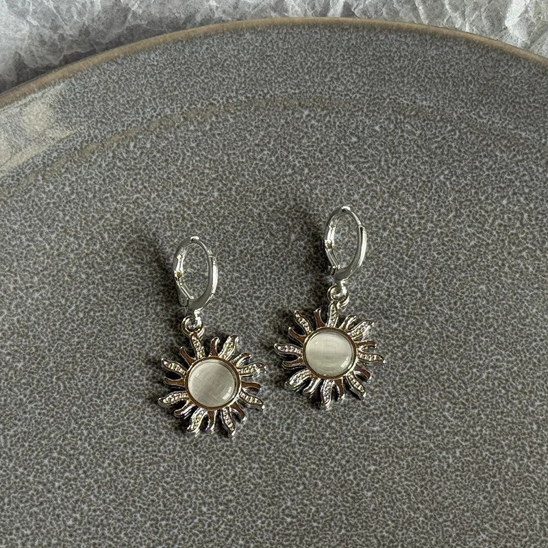 Silver stainless steel hoop earrings shaped like a sun and moon flower on a gray plate