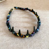 A black resin wave toothed headband made from multicolored yarn is displayed on a light brown surface.