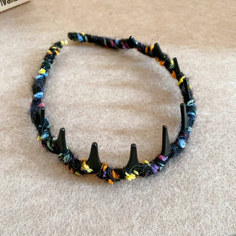 A black resin wave toothed headband made from multicolored yarn is displayed on a light brown surface.