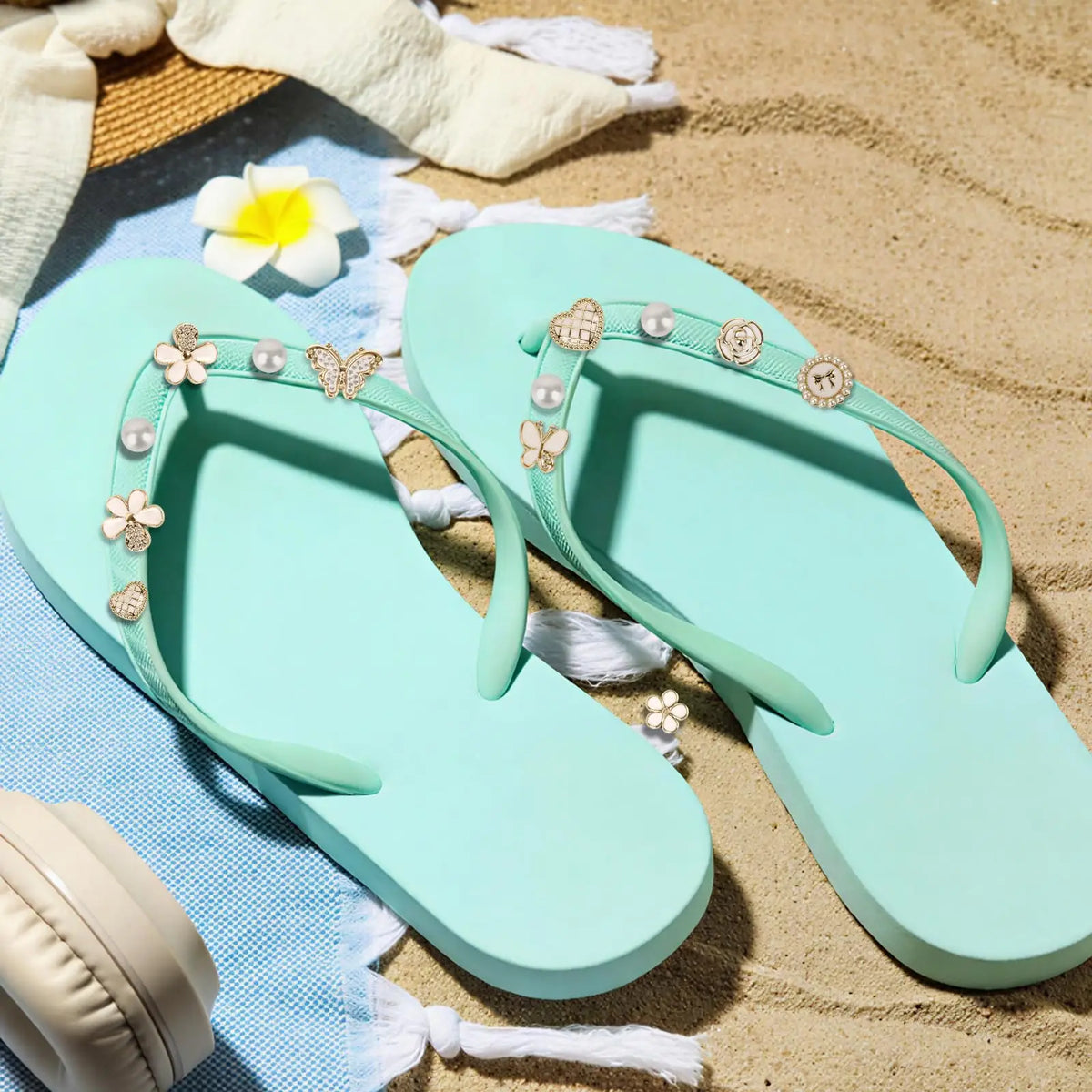 Sandalias tipo flip-flop verde menta claro con adornos de imitación de perla y oro sobre arena y tela azul.