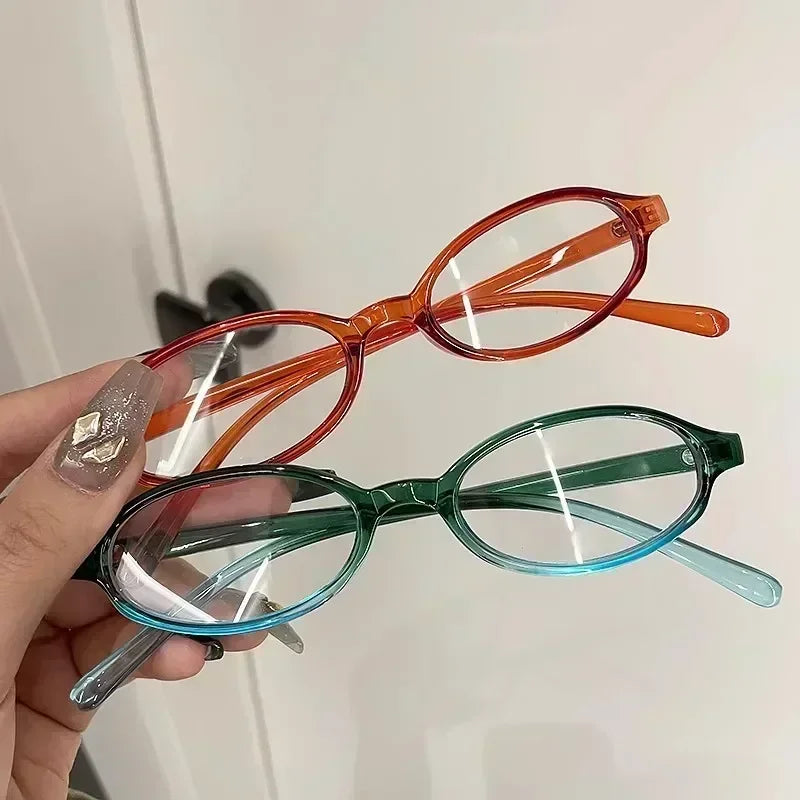 Une main tient des lunettes de mode ovales rétro Y2K avec des montures orange et sarcelle.