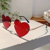 Rote herzförmige, randlose Sonnenbrille mit goldenen Akzenten auf weißem Untergrund.