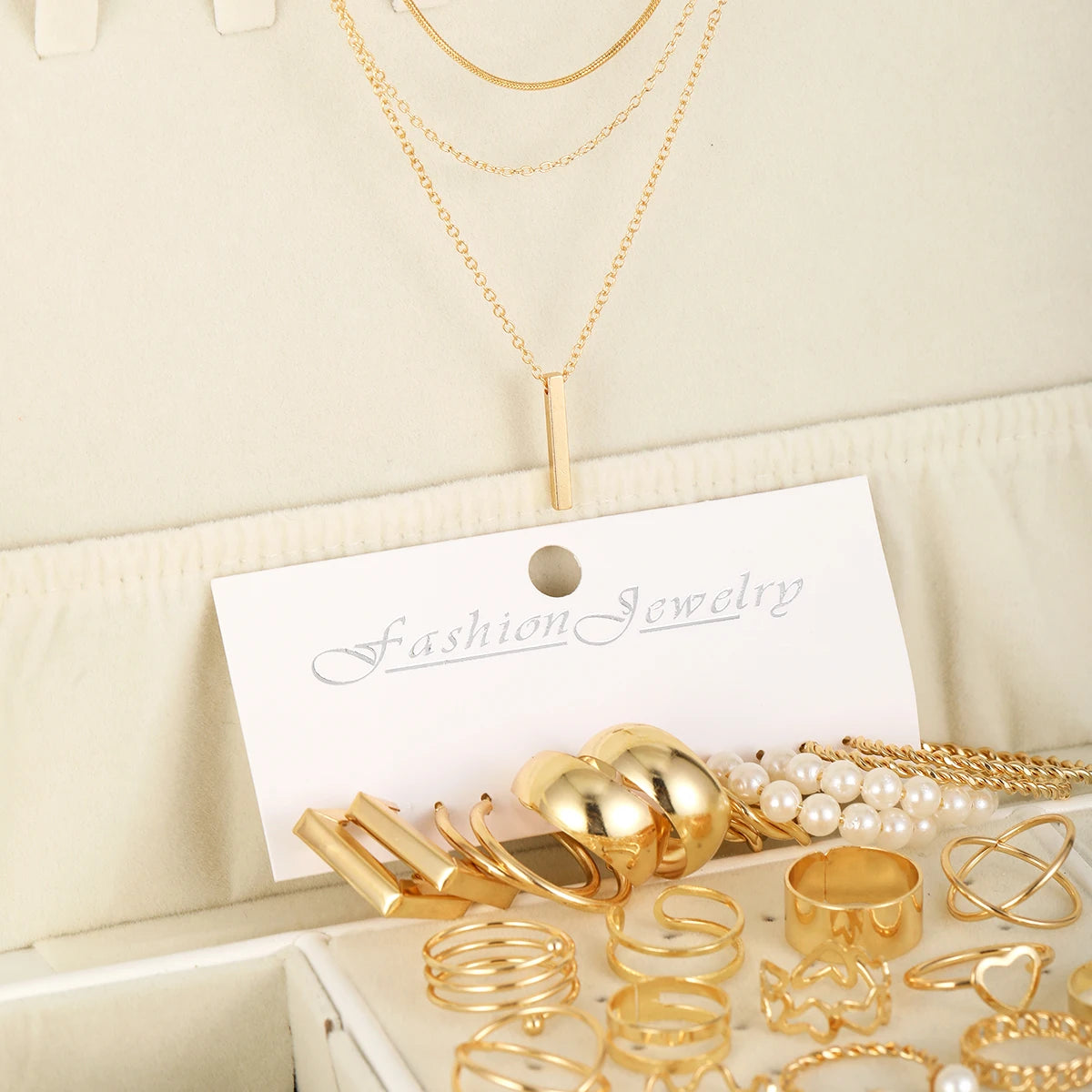 Collection de bijoux géométriques dorés bohèmes, colliers, bagues et bracelets, présentés sur une carte blanche.