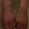 A close-up of two hands showing a gold-toned heart magnetic bracelet set for couples.