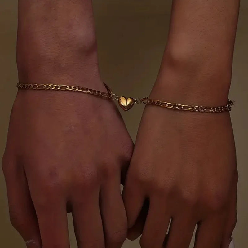 A close-up of two hands showing a gold-toned heart magnetic bracelet set for couples.