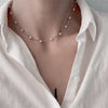 Gros plan d'un collier de perles minimaliste porté autour du cou sur un t-shirt blanc.