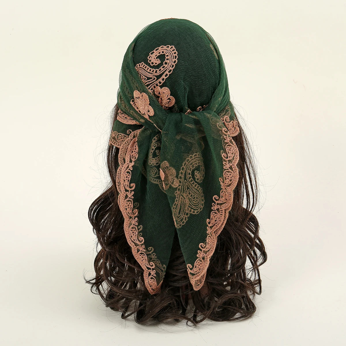 A dark green floral embroidered lace bandana headscarf tied around dark, curly hair.