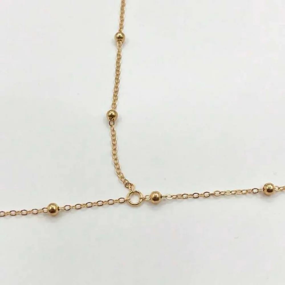 A delicate gold belly chain body jewelry necklace with small spherical beads.