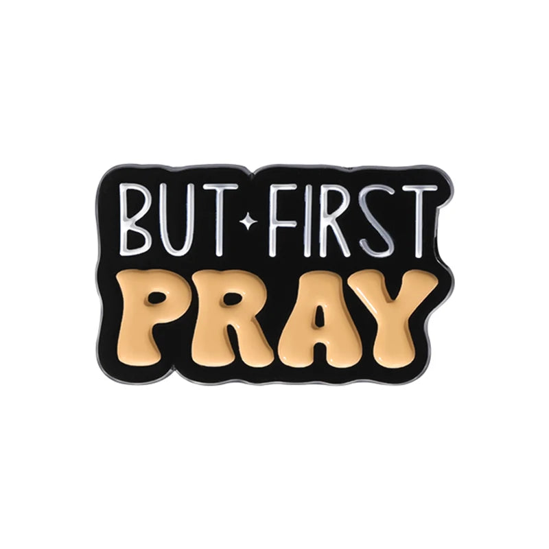 Broche émail noire avec lettres dorées indiquant BUT FIRST PRAY