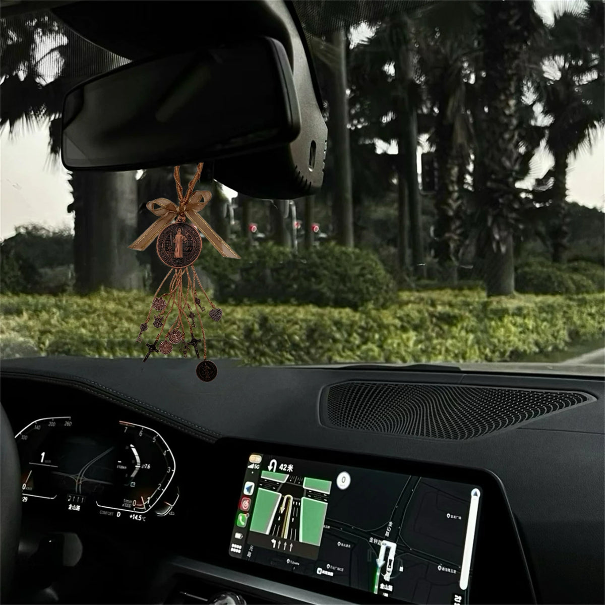 Interior view of a car dashboard showing a digital display and a hanging protection charm set.
