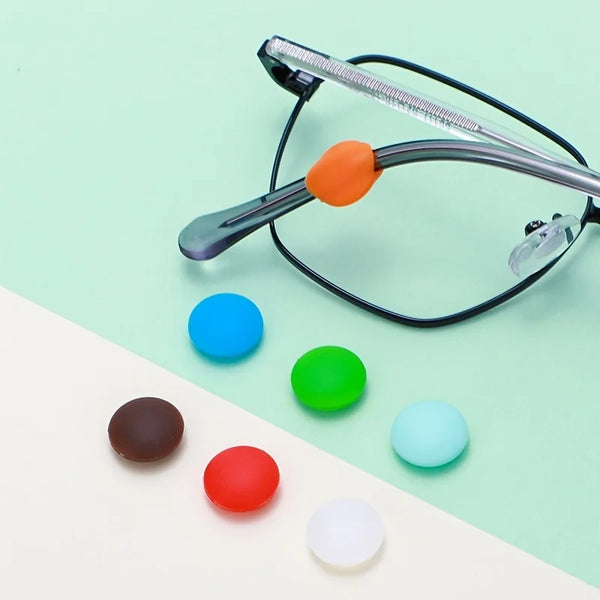 A pair of eyeglasses with silicone grips in orange, blue, green, red, and white colors resting on a white surface.
