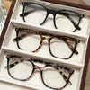 A set of classic square anti-blue light eyeglasses displayed in a brown box.