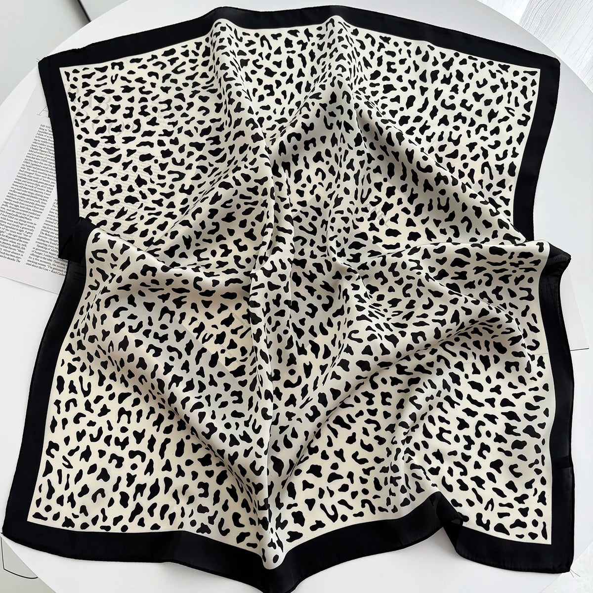 A folded luxury leopard print silk scarf featuring black and cream spots.