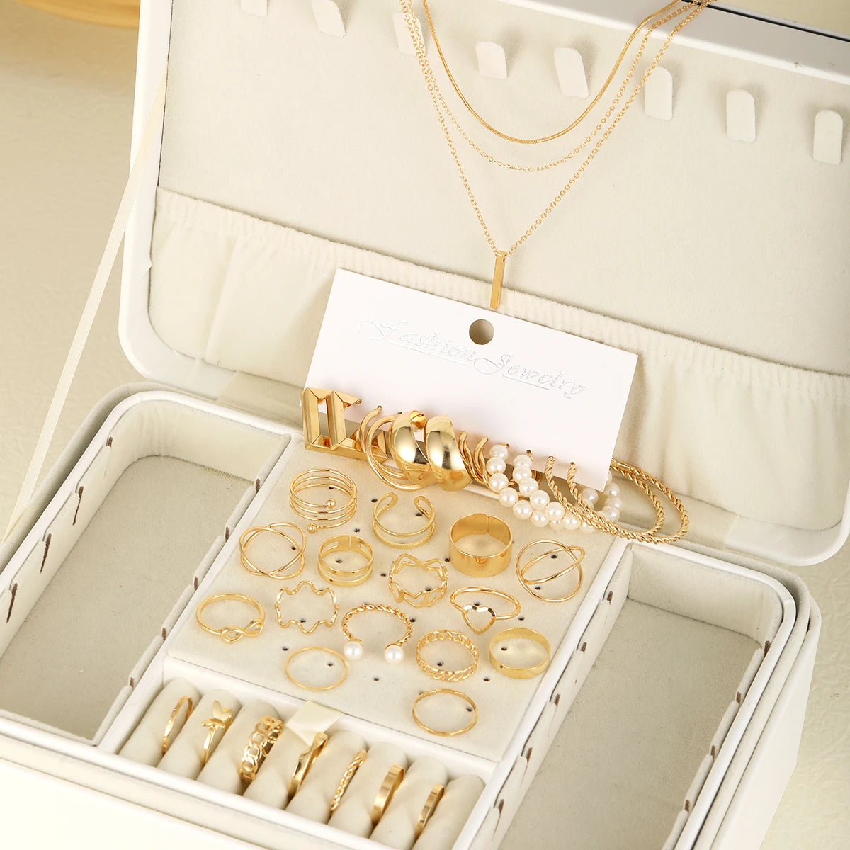 Collection de bijoux géométriques dorés bohèmes, bagues et colliers, présentés dans une boîte ouverte.