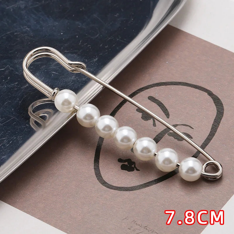 A silver safety pin with a string of white pearls is displayed on brown paper.