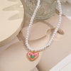 A delicate pearl necklace with a pink crystal heart pendant displayed on a neutral background.