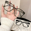 A hand holds a pair of elegant geometric reading glasses with brown and black leopard print frames.