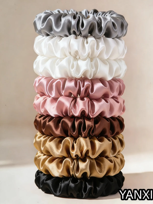 A stack of five satin hair scrunchies in various shades including gray, white, pink, brown, and black.