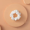 Un lazo de cabello de seda blanca con forma de lazo espolvoreado, centrado sobre un fondo circular melocotón claro.