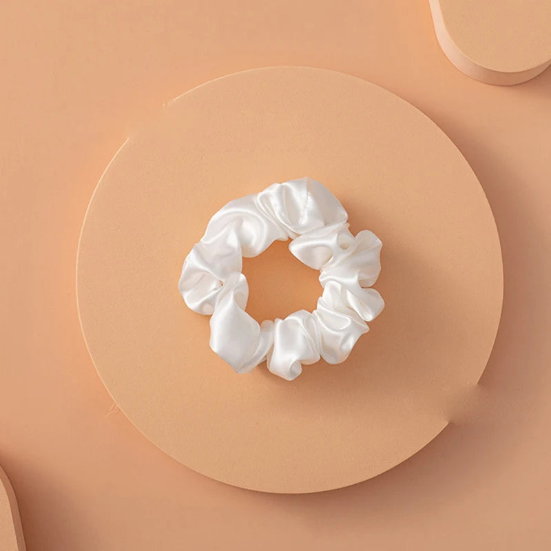 Un lazo de cabello de seda blanca con forma de lazo espolvoreado, centrado sobre un fondo circular melocotón claro.