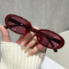 A hand holds a pair of maroon cat eye sunglasses with dark frames against a light background.