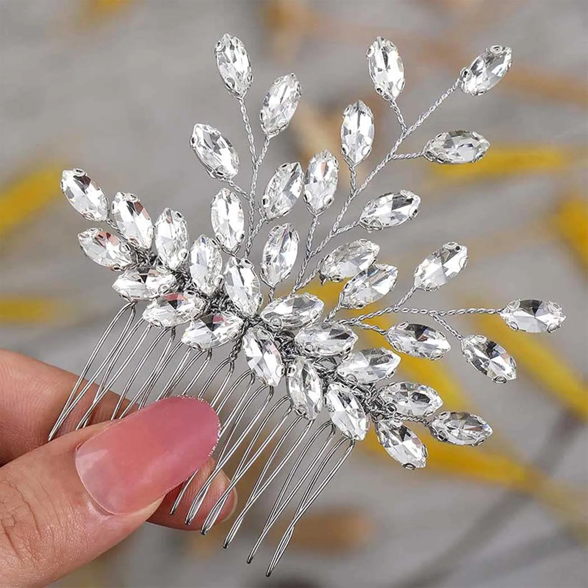 Une main tient un peigne de cheveux pour mariée en cristal avec des pointes d'argent délicates et des éléments floraux clairs