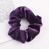 A close-up shot of a deep purple velvet scrunchie resting on a white surface.