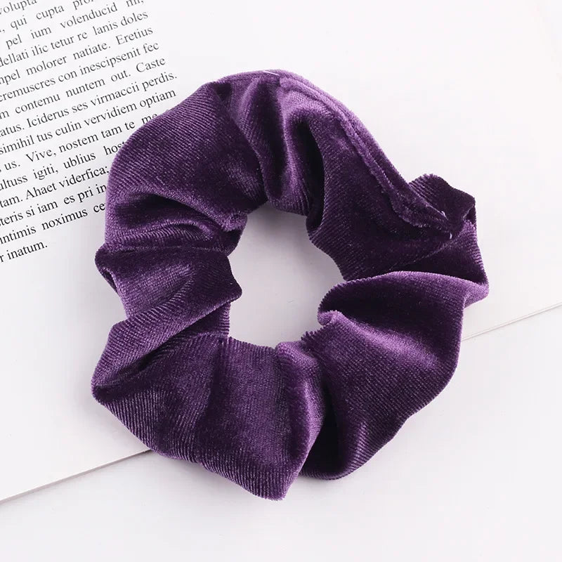 A close-up shot of a deep purple velvet scrunchie resting on a white surface.