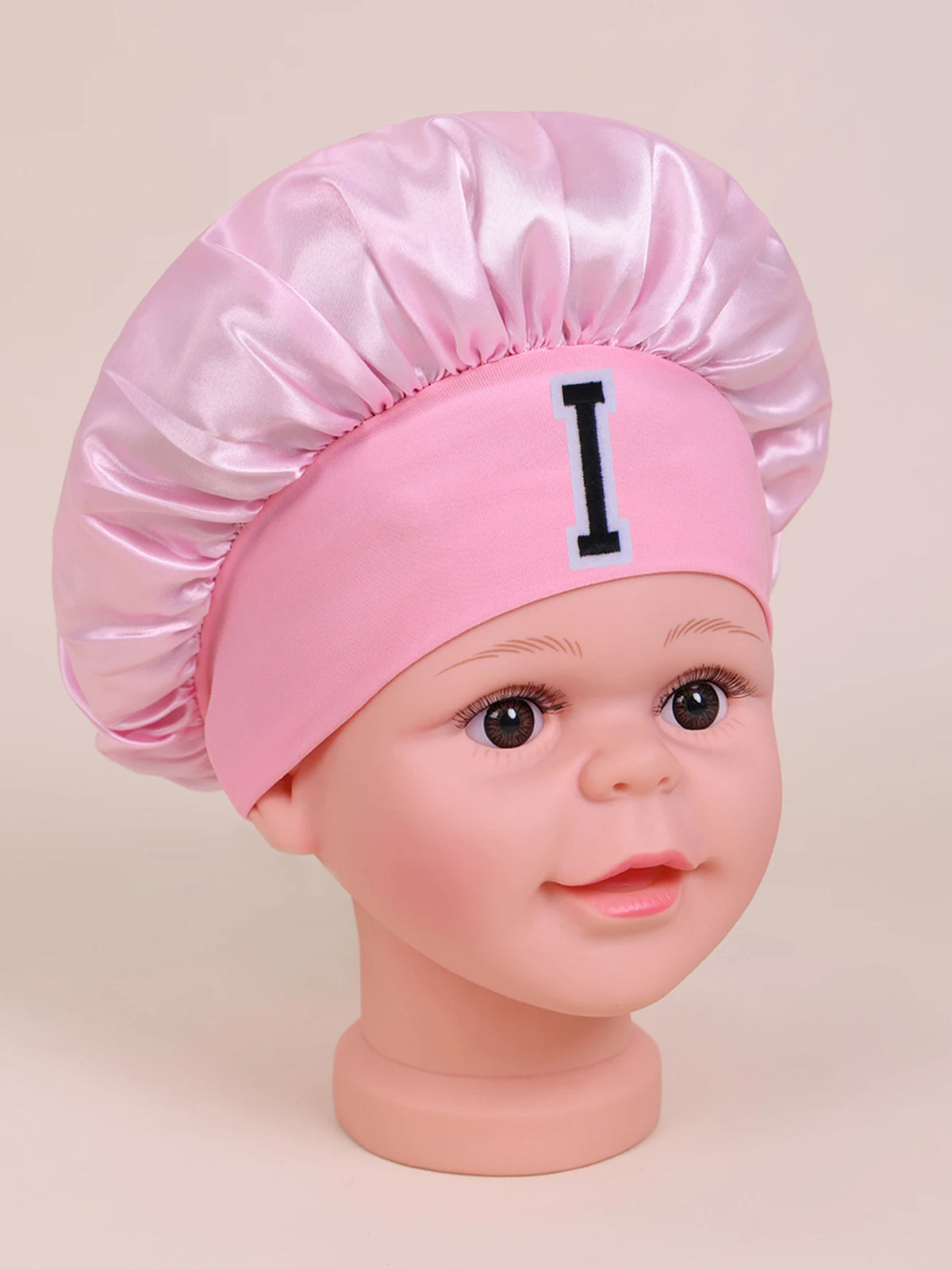 Pink satin sleep cap for kids with a black letter I embroidered on the front