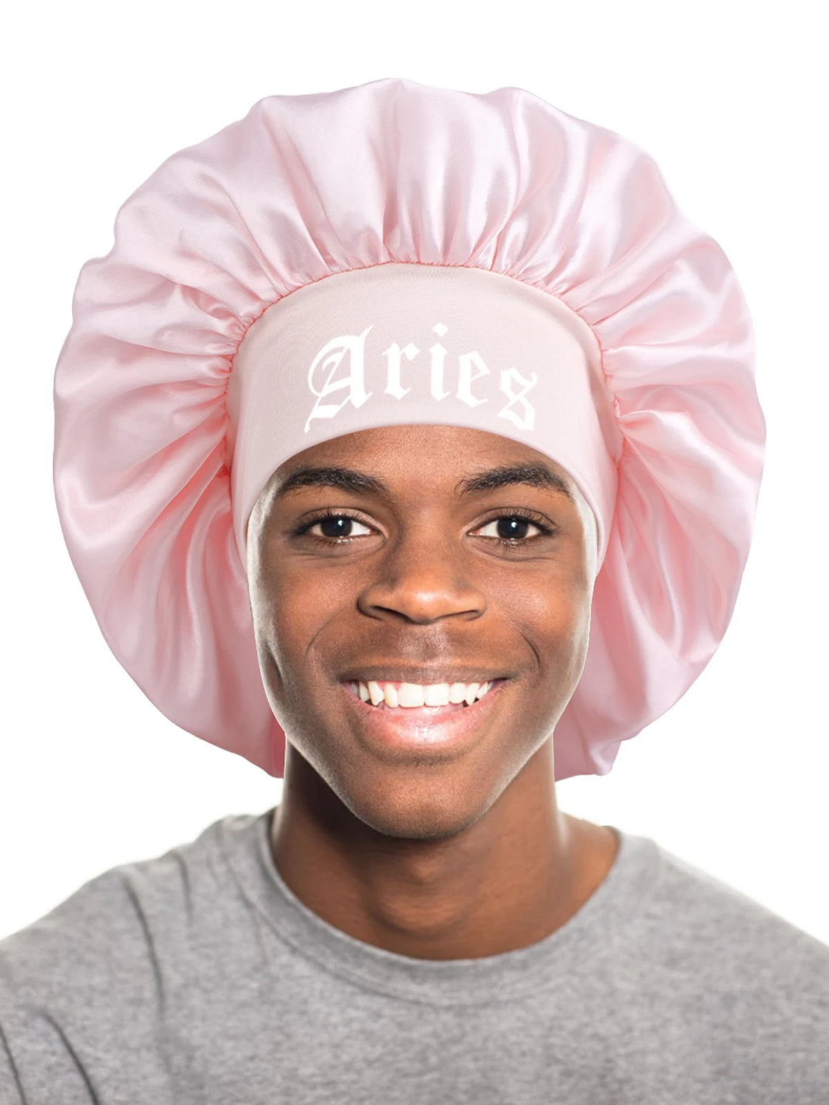 A young man wearing a pink satin sleep bonnet with an Aries wrap band and a gray t-shirt.