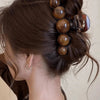 A close-up of a woman's dark brown hair styled in an elegant updo with acrylic pearl hair claw clips.