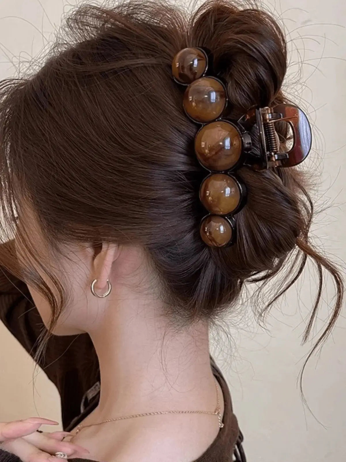 A close-up of a woman's dark brown hair styled in an elegant updo with acrylic pearl hair claw clips.