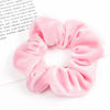 A close-up of six soft pink velvet scrunchies for hair ties arranged in a circular shape.