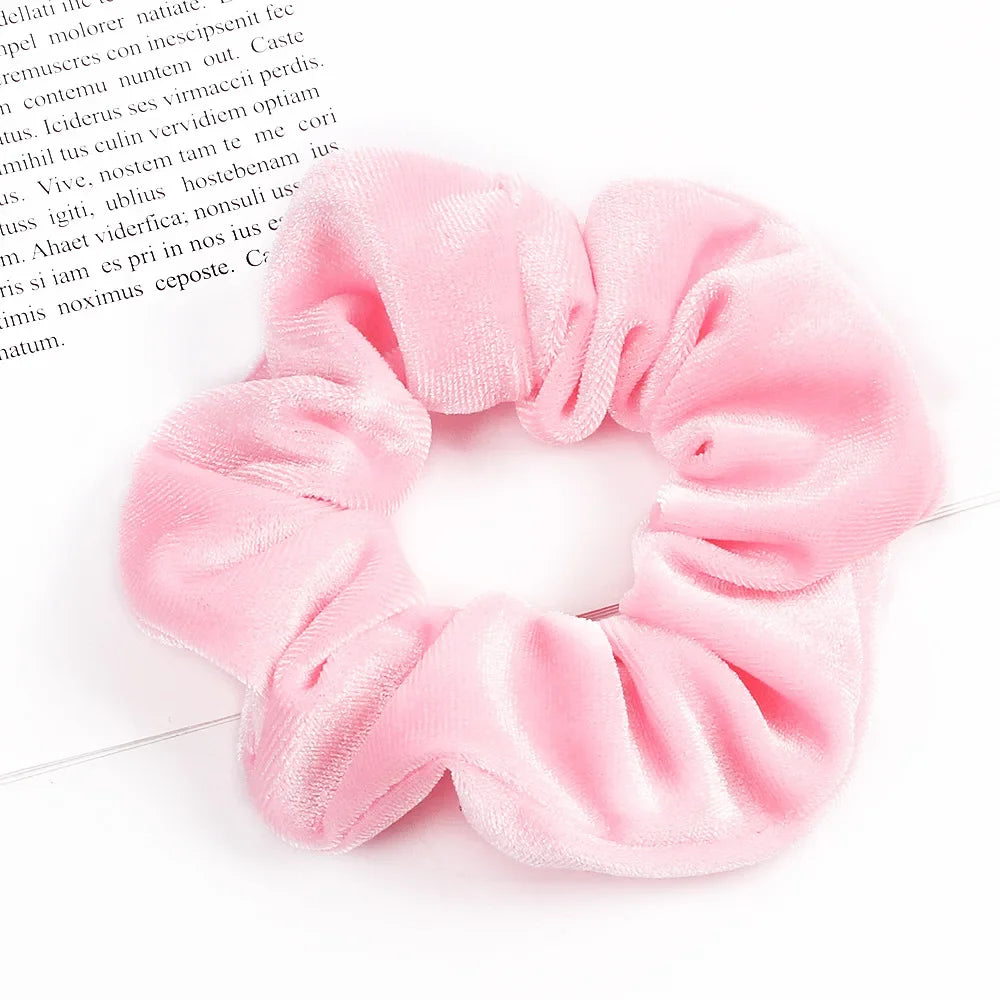 A close-up of six soft pink velvet scrunchies for hair ties arranged in a circular shape.