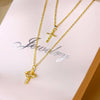 Collier doré avec pendentif de lettre et croix sur fond blanc.