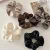 A collection of five elegant silk scrunchie hair ties in shades of beige, brown, and black.