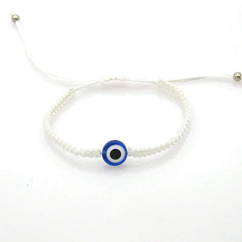 A white beaded bracelet with a blue and black evil eye charm.
