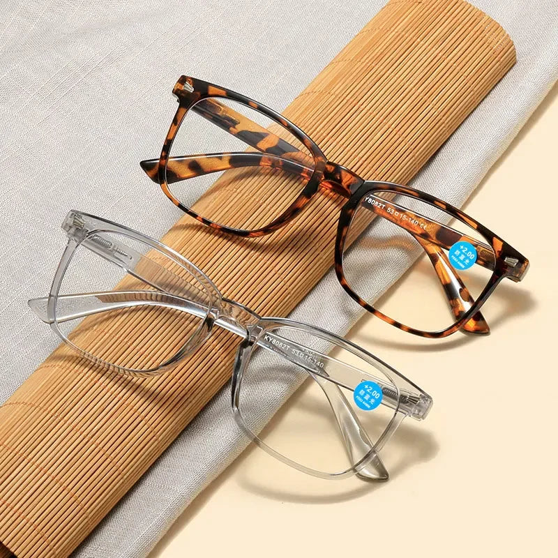 Un par de gafas de lectura de capitoné sobre un fondo beige junto a un paño enrollado.