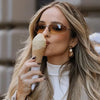 Eine Frau mit langen blonden Haaren hält eine Eiscreme und trägt ovale, frameless Y2K-Sonnenbrillen.