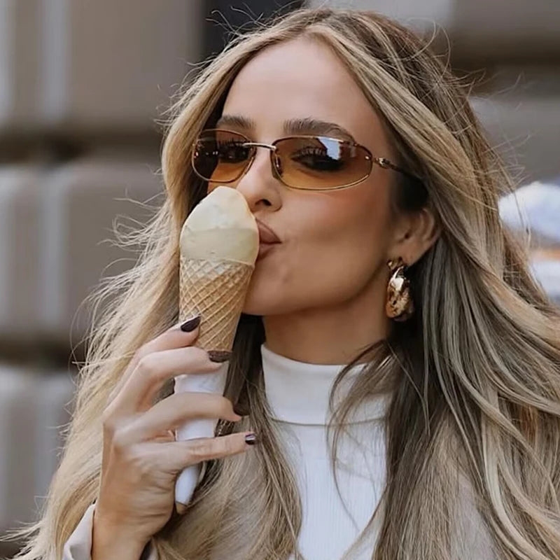 Eine Frau mit langen blonden Haaren hält eine Eiscreme und trägt ovale, frameless Y2K-Sonnenbrillen.