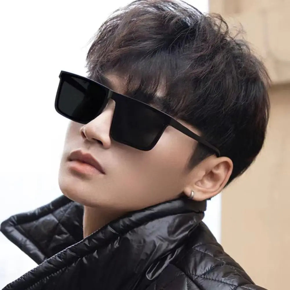 A close-up of a person wearing black square frame sunglasses and a black quilted jacket.