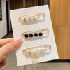 Gold-toned brooch pins featuring pearl and black gemstone embellishments displayed on a white card.