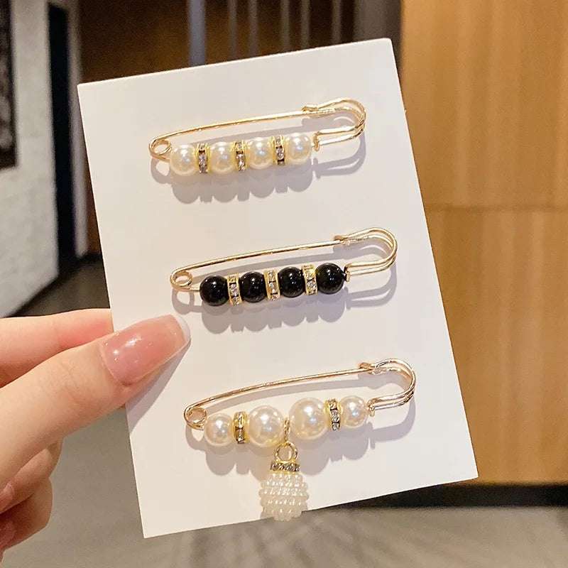 Gold-toned brooch pins featuring pearl and black gemstone embellishments displayed on a white card.