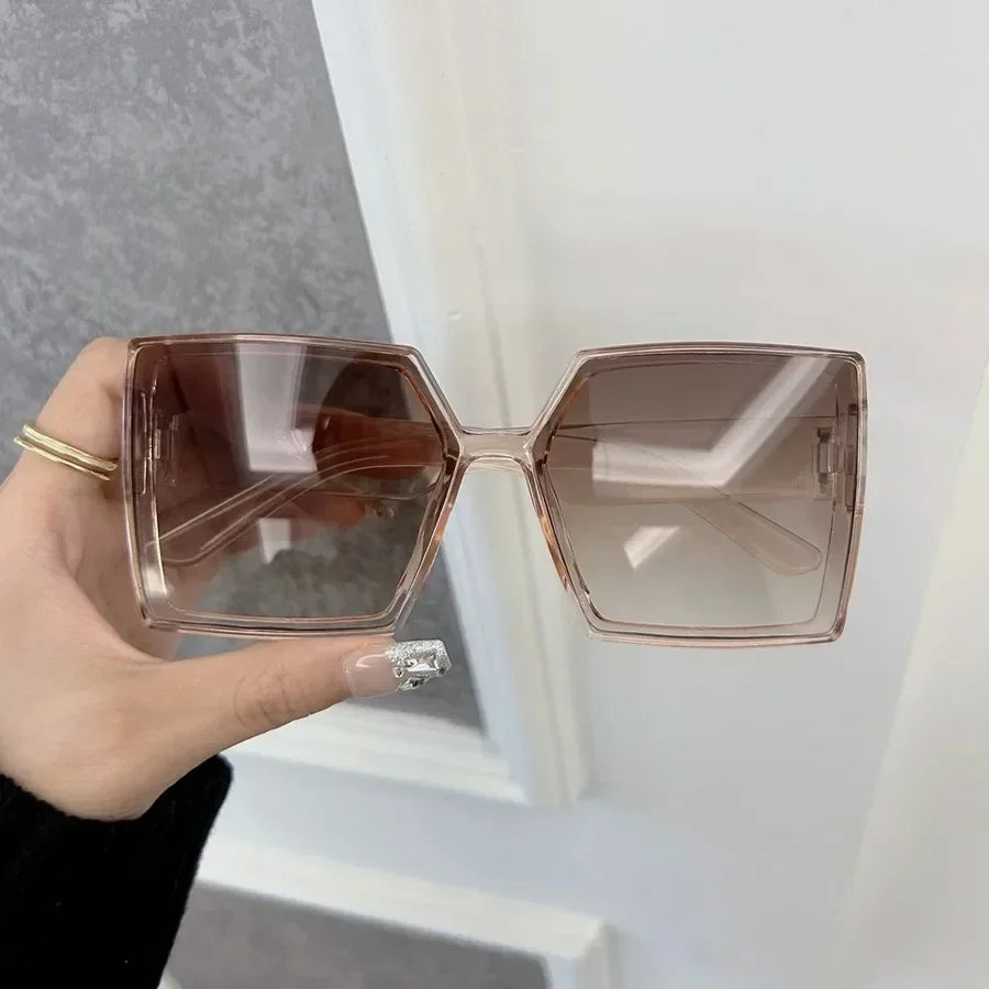 A pair of rose gold mirror square sunglasses held by a hand against a white background.