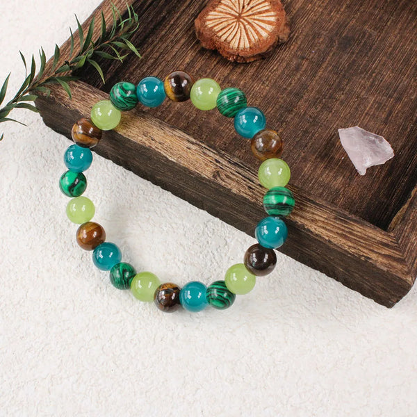 A bracelet made of natural stone beads in shades of green and blue is displayed on a wooden surface.